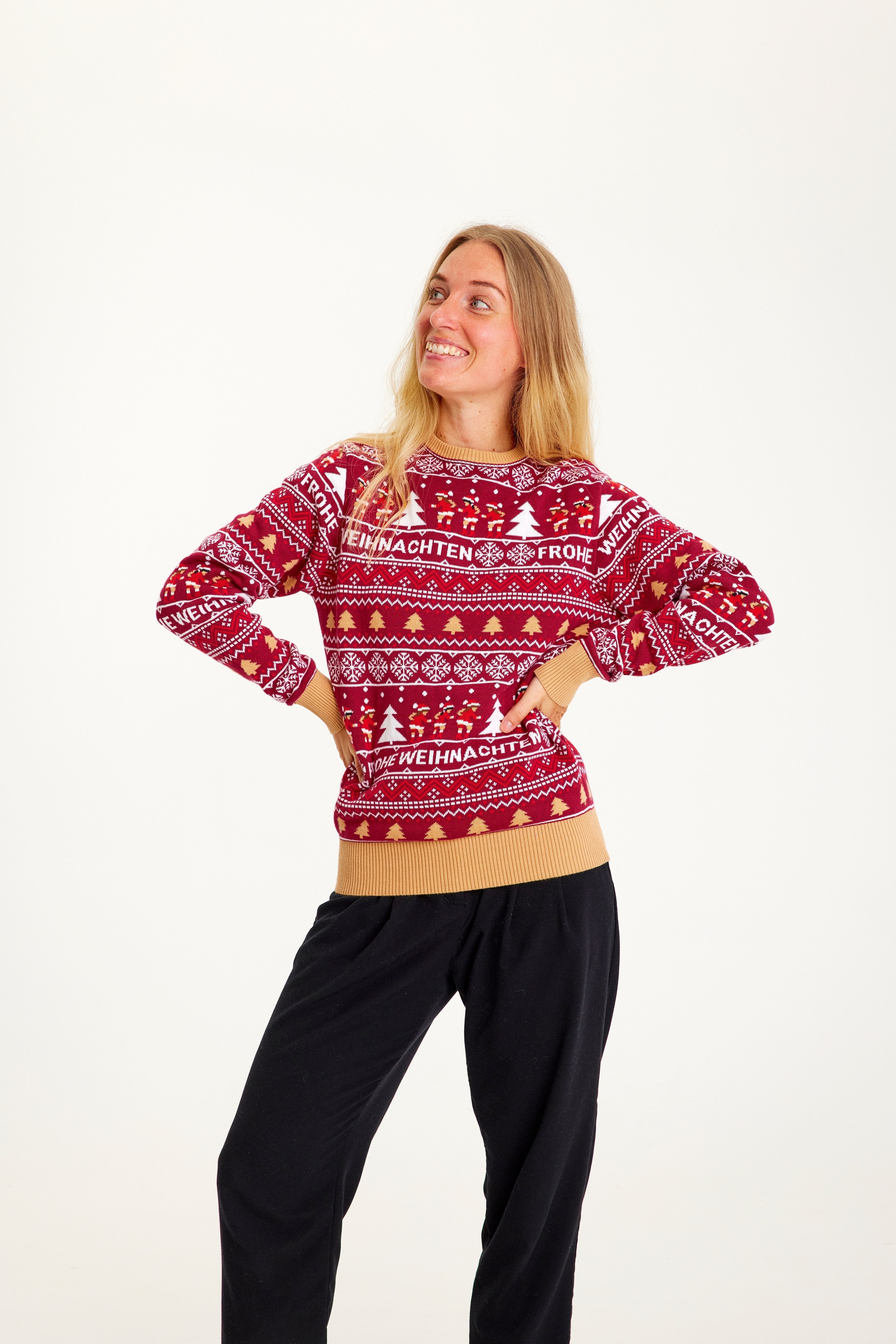 Een vrouw poseert terwijl ze een rode kersttrui draagt met kerstbomen erop.